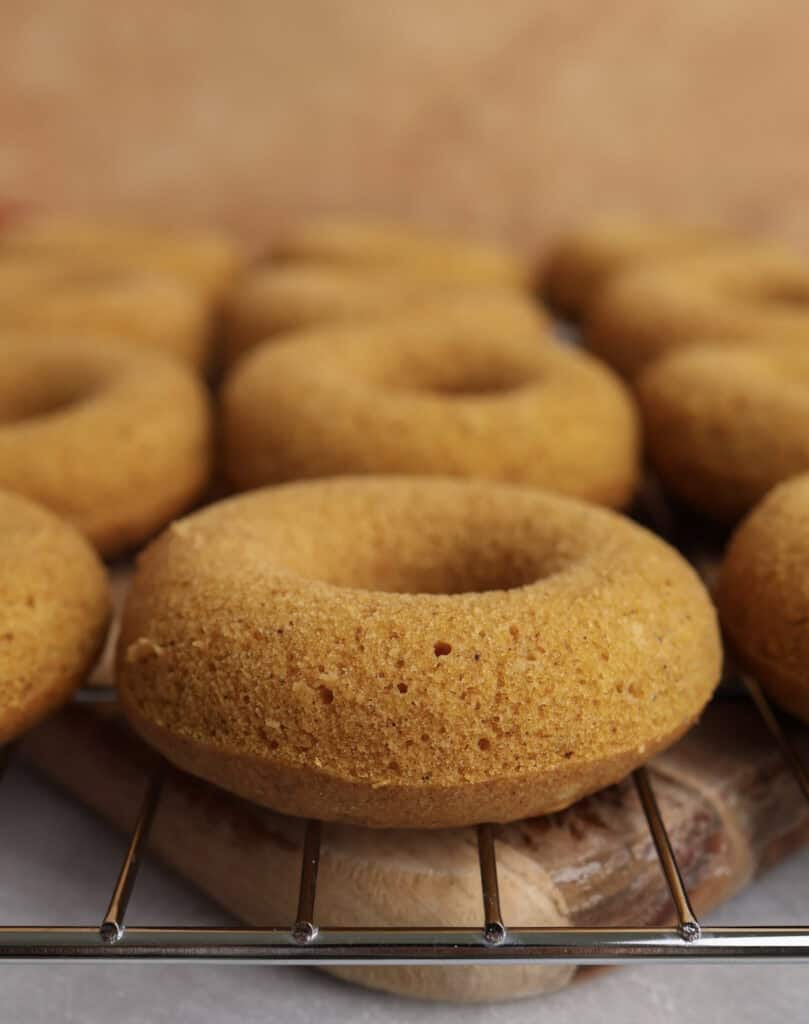 Baked pumpkin donuts sitting a cooling rack.