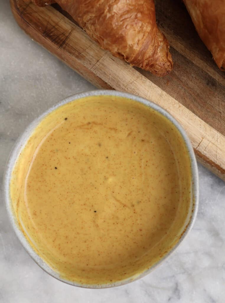 Homemade spicy honey mustard in a bowl next to a croissant.