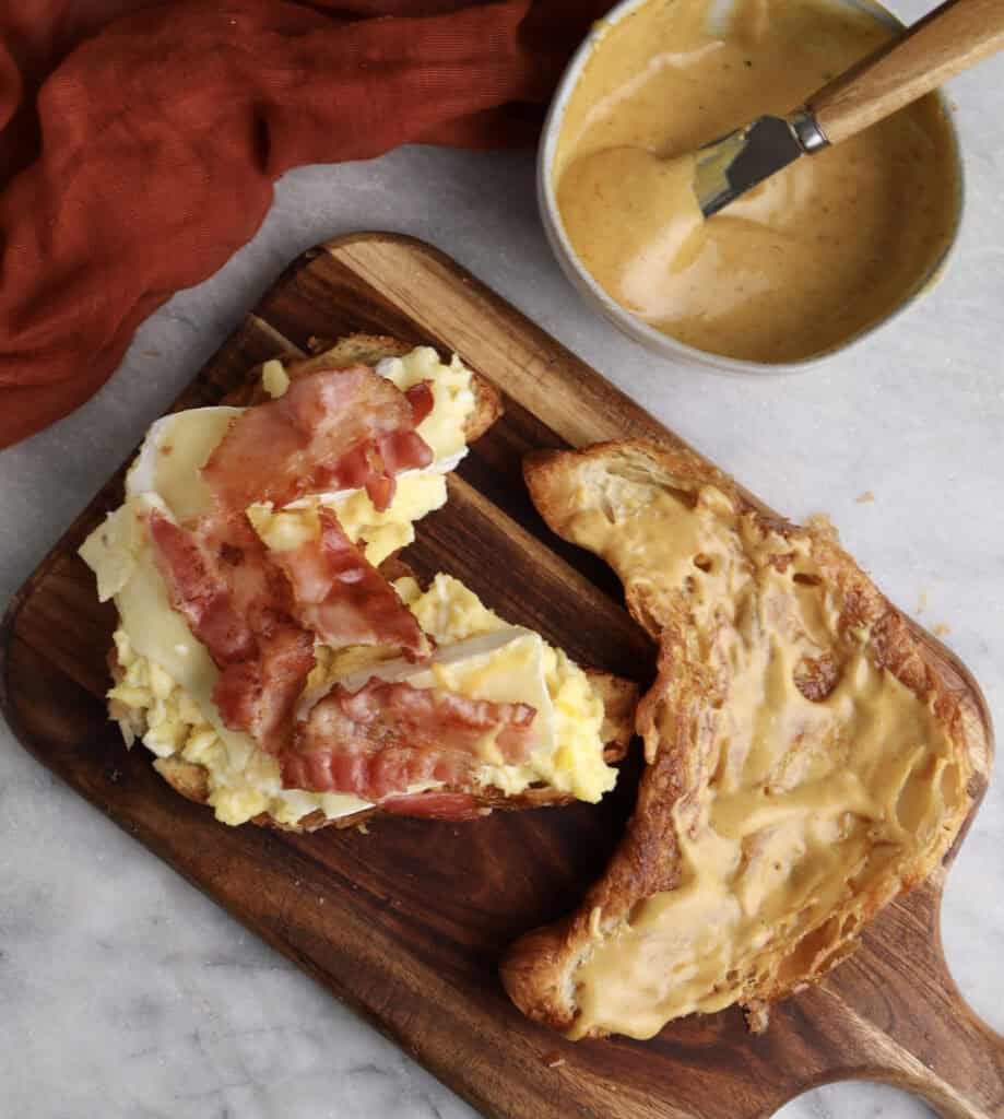 Breakfast croissant sandwich open faced, showing the spicy honey mustard, brie cheese, scrambled eggs and bacon.