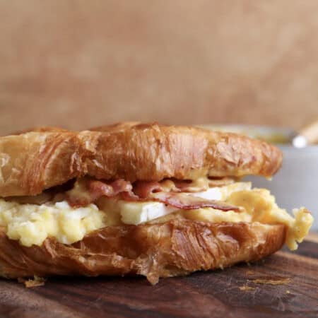 Breakfast croissant sandwich with bacon, egg, brie and spicy honey mustard on cutting board.