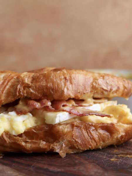 Breakfast croissant sandwich with bacon, egg, brie and spicy honey mustard on cutting board.