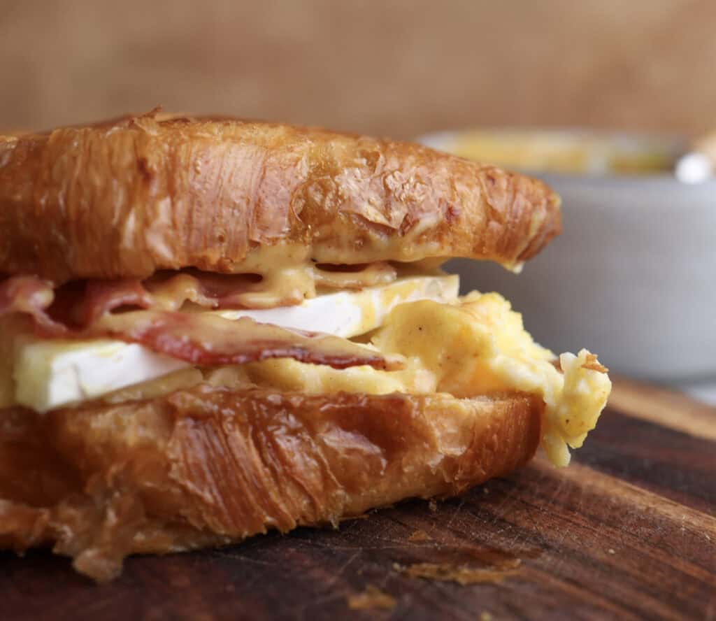 Up close side view of the croissant breakfast sandwich with brie cheese, eggs and bacon.