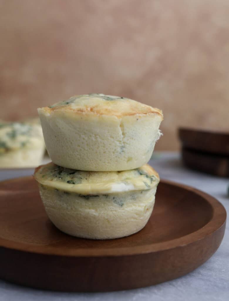 Two cottage cheese egg bites with spinach stacked on each other on a wood plate.