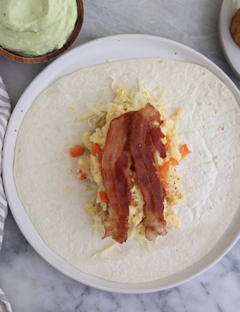 Open tortilla with fillings in the center for the breakfast burrito.