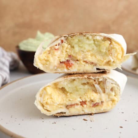 Breakfast burritos cut open and stacked on each other, showing layers of eggs, hash browns, bacon and cheese.