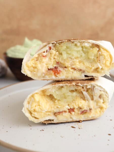 Breakfast burritos cut open and stacked on each other, showing layers of eggs, hash browns, bacon and cheese.