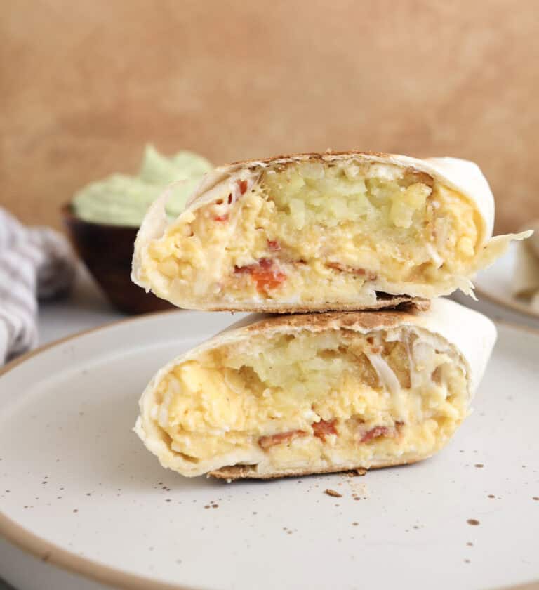 Breakfast burritos cut open and stacked on each other, showing layers of eggs, hash browns, bacon and cheese.
