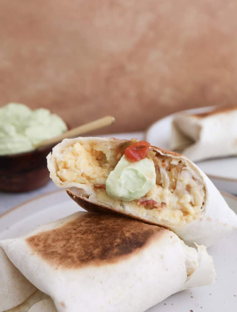 Breakfast burrito cut open with spicy avocado crema dollop.