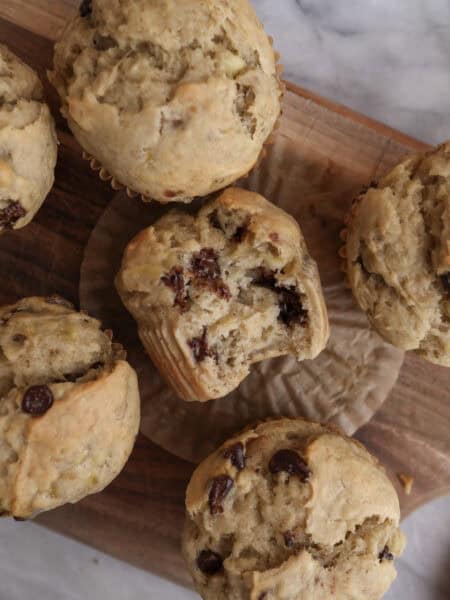Banana Chocolate Chip muffins with one with bite on a cutting board.