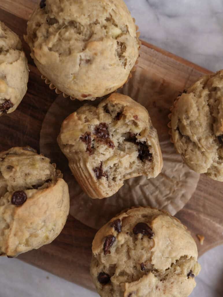 Banana Chocolate Chip muffins with one with bite on a cutting board.