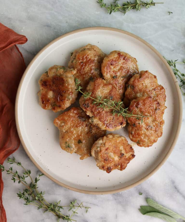 Homemade Chicken Sausage Patties stacked on a plate with a sprig of fresh thyme on top.
