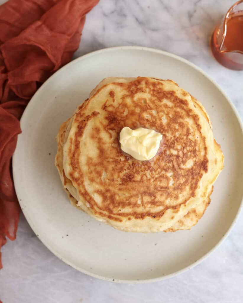 Over head view of a stack of Greek yogurt pancakes on plate with a pat of butter on top.