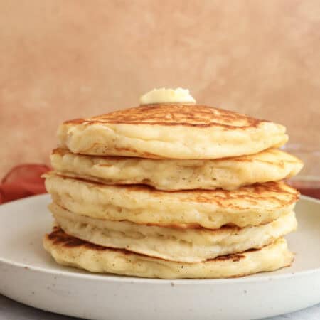 Stack of Greek yogurt pancake with brown butter on a plate with a pat of butter om top.