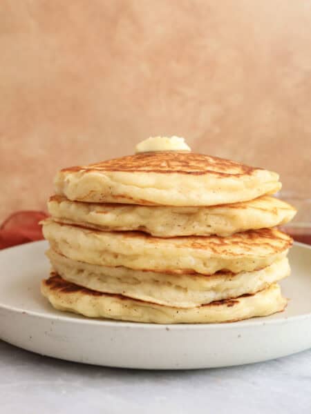 Stack of Greek yogurt pancake with brown butter on a plate with a pat of butter om top.