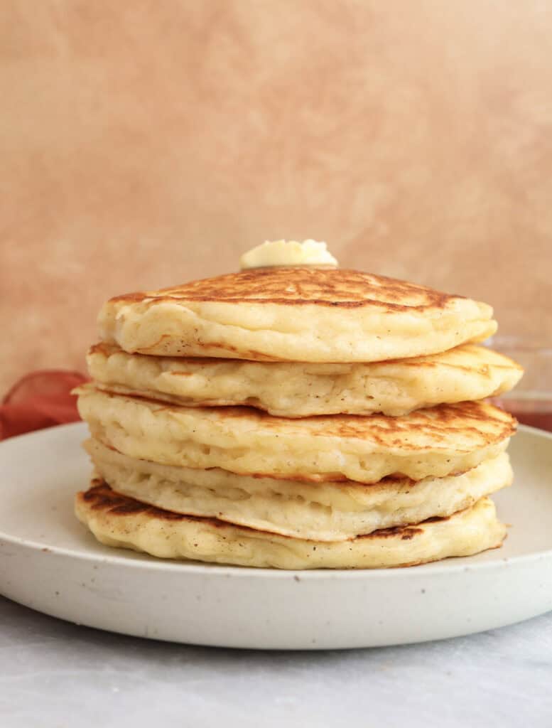 Stack of Greek yogurt pancake with brown butter on a plate with a pat of butter om top.