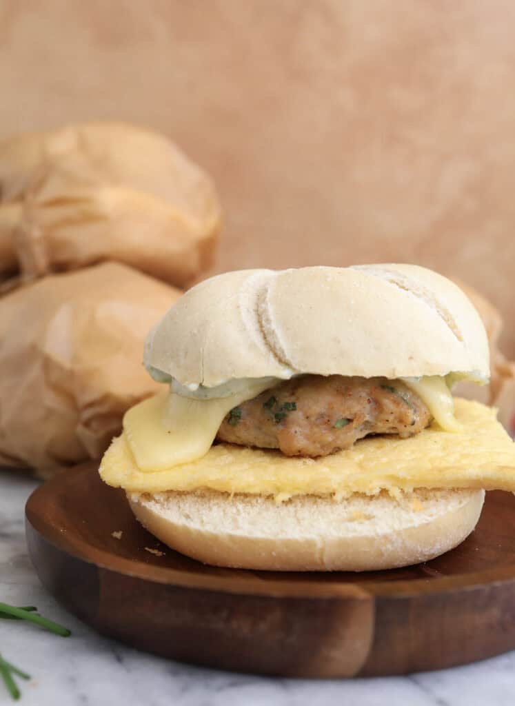 A side view of the egg, sausage and cheese sandwich on a wood plate.
