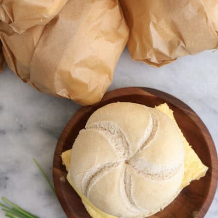 A egg and sausage breakfast sandwich on a plate with sandwiches wrapped in parchment paper next to the plate ready to go in the freezer.