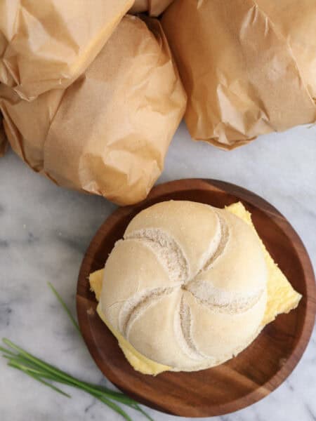 A egg and sausage breakfast sandwich on a plate with sandwiches wrapped in parchment paper next to the plate ready to go in the freezer.