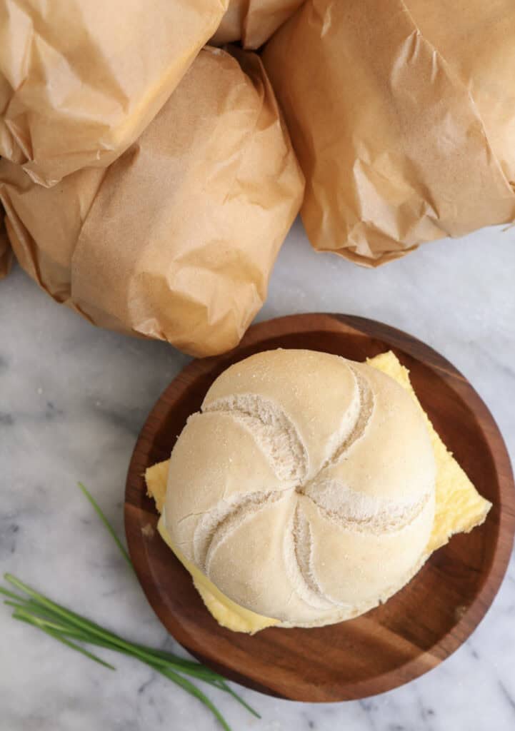 A egg and sausage breakfast sandwich on a plate with sandwiches wrapped in parchment paper next to the plate ready to go in the freezer.
