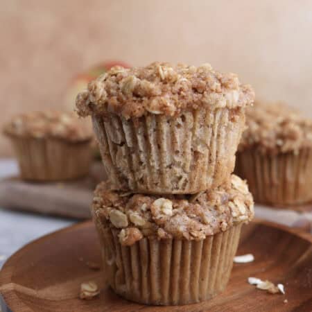 Two apple oat muffins stacked on each other on a wood plate.
