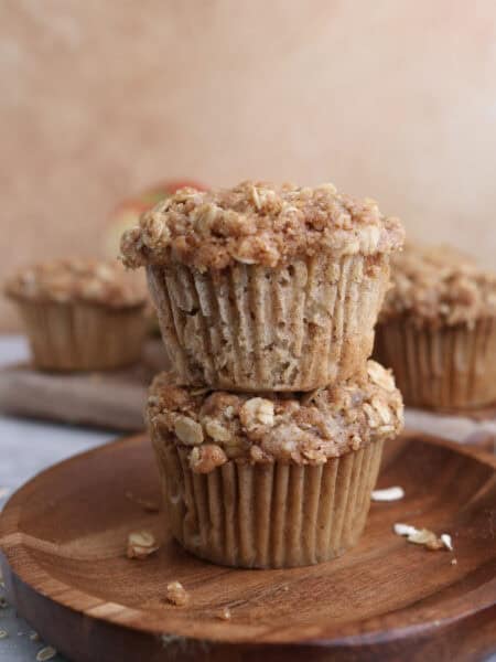 Two apple oat muffins stacked on each other on a wood plate.