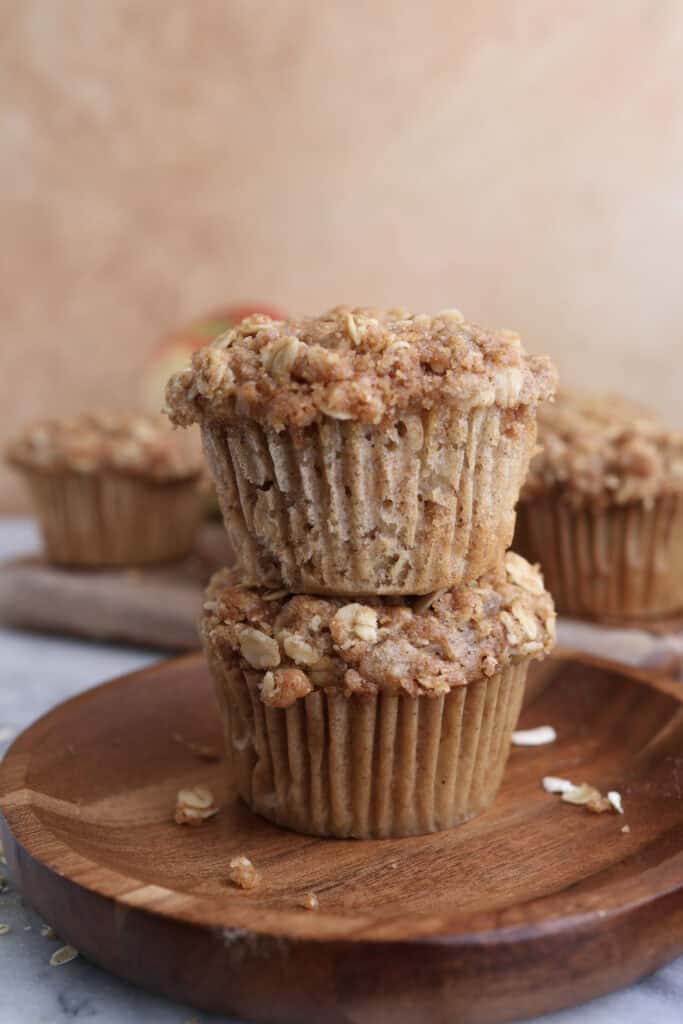 Two apple oat muffins stacked on each other on a wood plate.