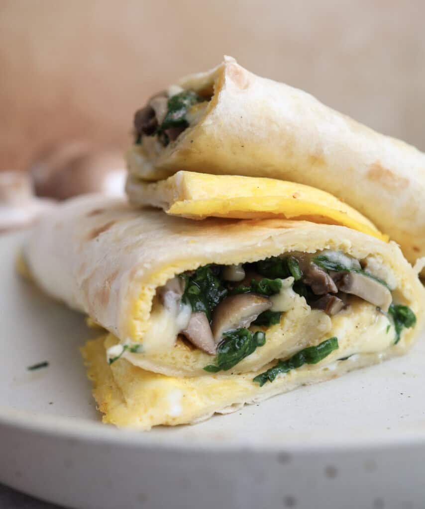 Up close of the egg wrap with mushroom and gouda cut open on a plate.