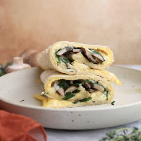 Breakfast egg wrap cut in half and stacked on each other, showing the layers of egg, mushrooms and gouda cheese in the middle.