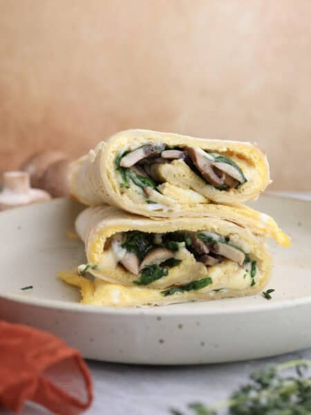 Breakfast egg wrap cut in half and stacked on each other, showing the layers of egg, mushrooms and gouda cheese in the middle.