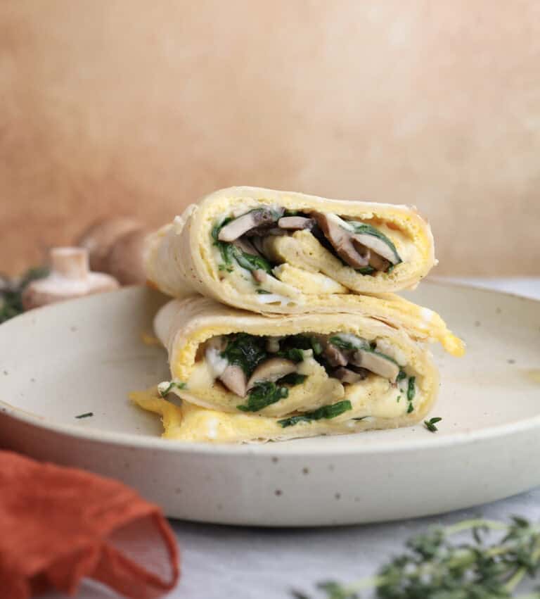 Breakfast egg wrap cut in half and stacked on each other, showing the layers of egg, mushrooms and gouda cheese in the middle.