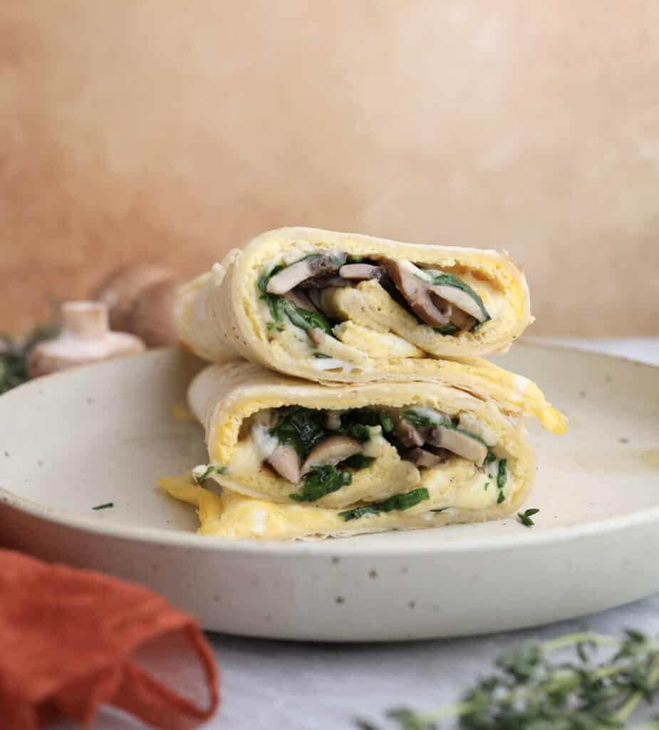 Breakfast egg wrap cut in half and stacked on each other, showing the layers of egg, mushrooms and gouda cheese in the middle.