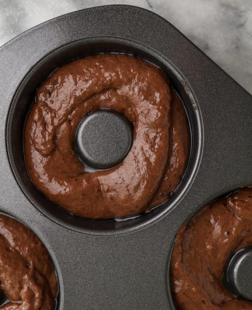 Chocolate donut batter in a donut tin.