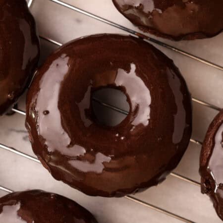 Chocolate protein baked donut just coated with chocolate glaze on a cooling rack.