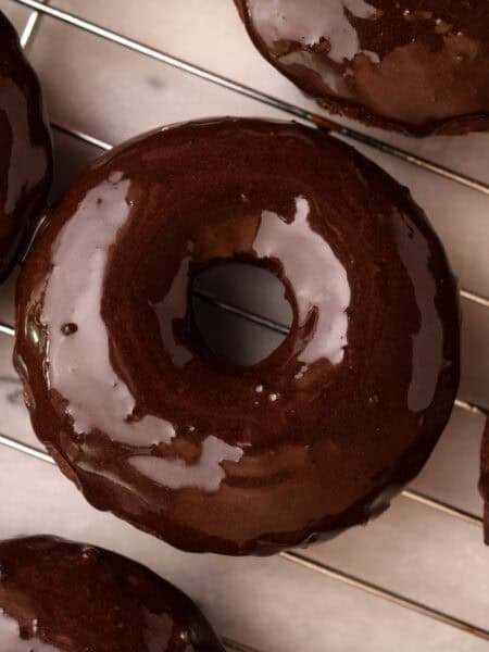 Chocolate protein baked donut just coated with chocolate glaze on a cooling rack.