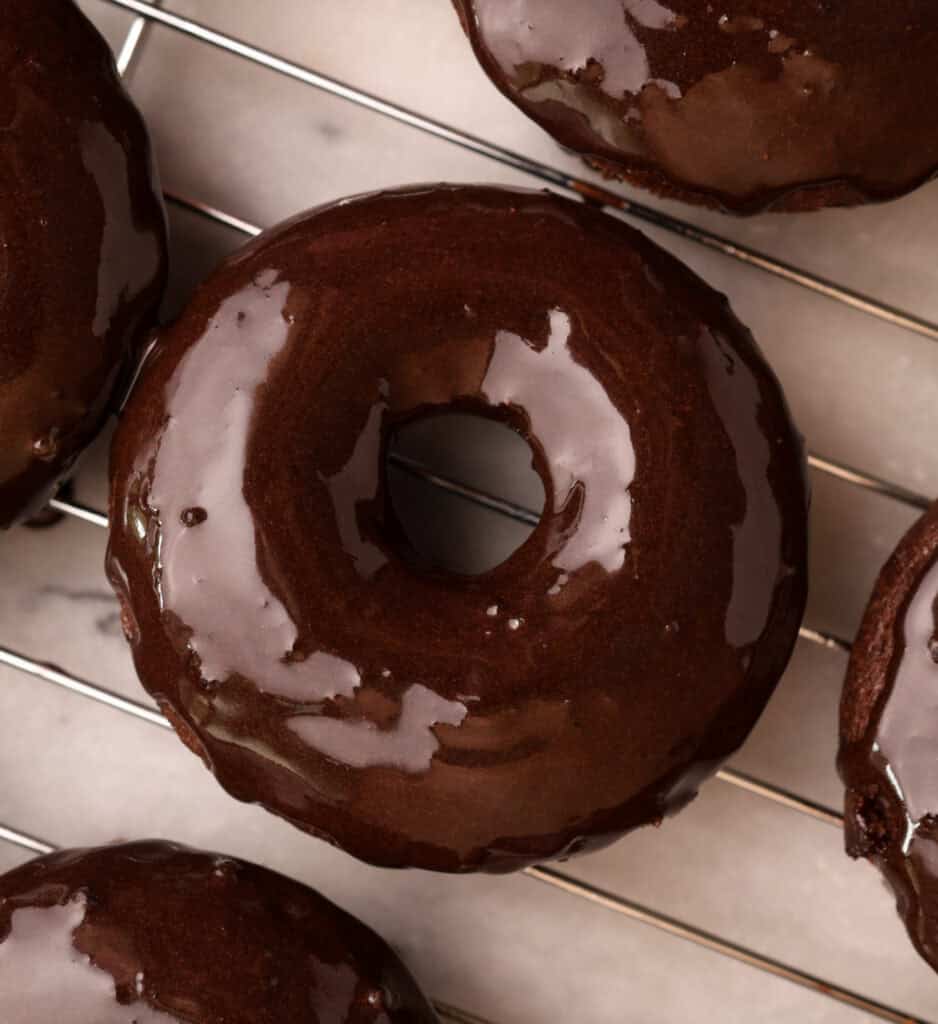 Chocolate protein baked donut just coated with chocolate glaze on a cooling rack.