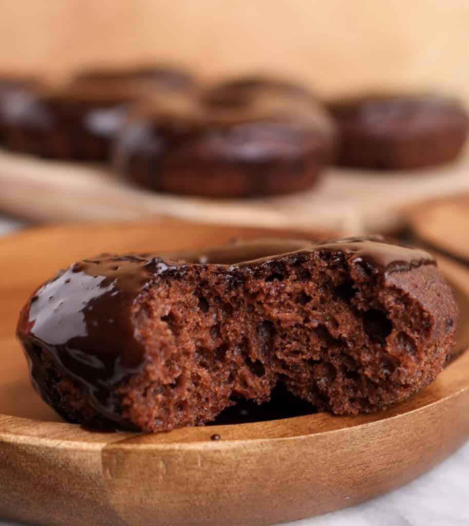 Chocolate baked donut with chocolate glaze on a wood plate with a bite missing.