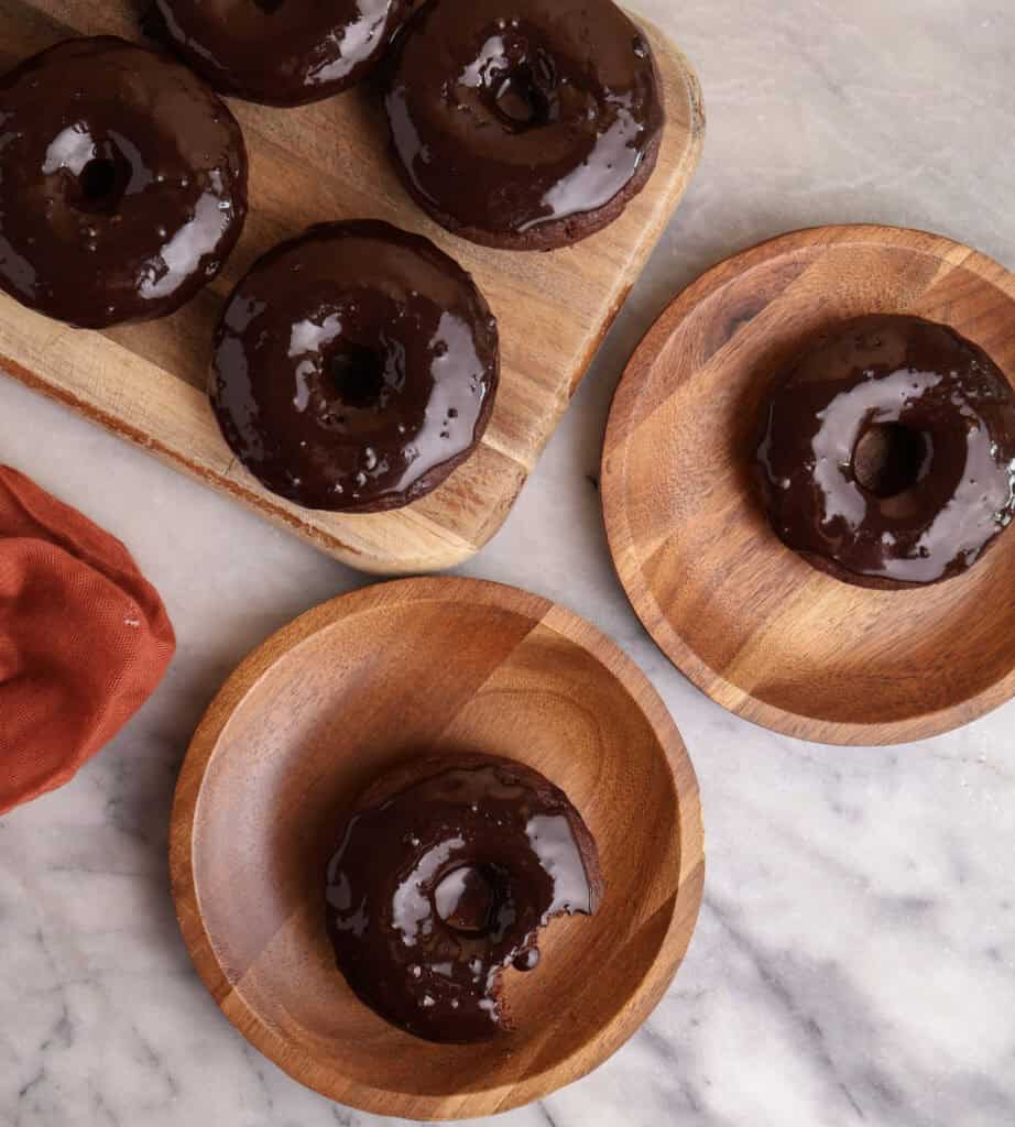 Chocolate baked donuts on wood plates, with one a bite taken out of the donut.