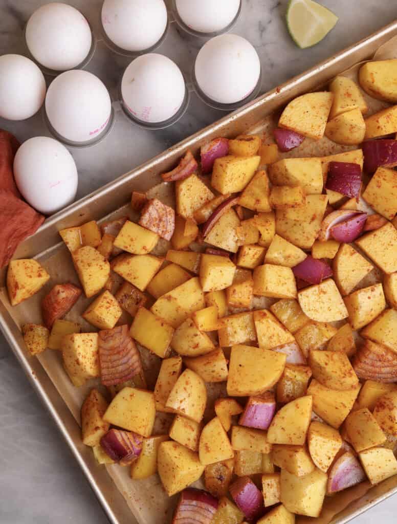 Breakfast potatoes with onions, bell pepper, and seasoning on a baking sheet before going in the oven.