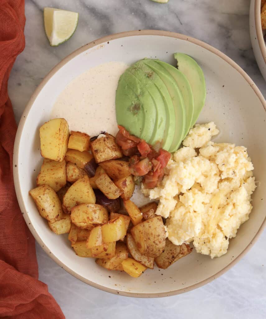 plated breakfast potato bowls with potatoes, cottage cheese scrambled eggs, sliced avocado, salsa and chipotle sauce.