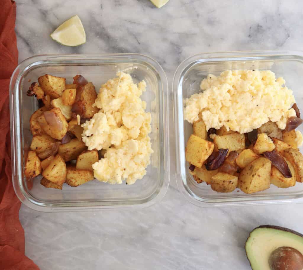 Roasted potatoes and cottage cheese scrambled eggs in storage containers for breakfast potato bowl meal prep.