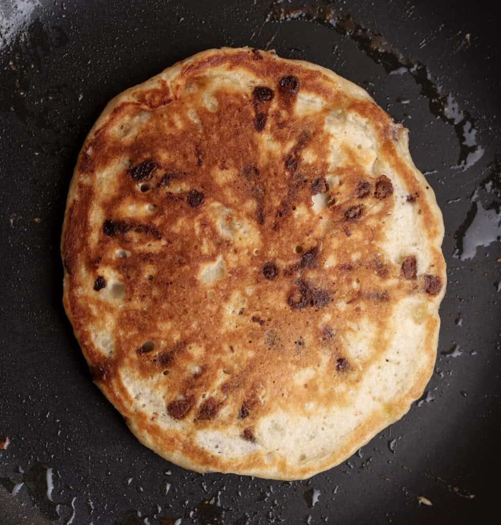Banana pancake in skillet, showing the brown edges after flipping.