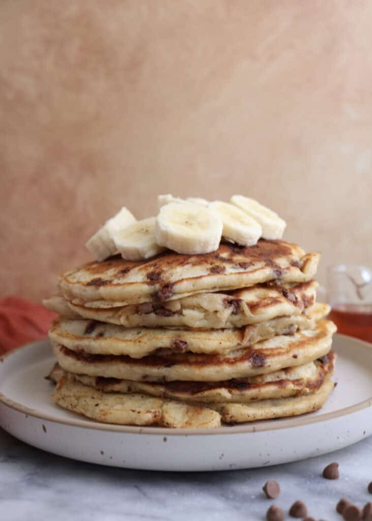 Stack of banana pancakes on a plate topped with banana slices.