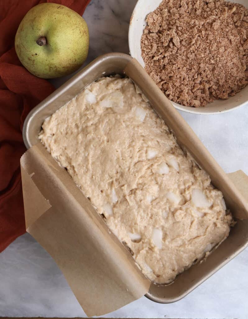 Pear bread batter in a loaf pan with the crumble in a bowl next to it. 