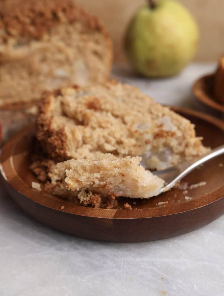 Slice of pear bread on a plate with a fork holding a piece of the bread. 