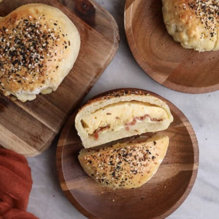 Breakfast pockets sitting on wood plates, with one cut open, showing the middle stuffed with eggs, bacon and cheese.