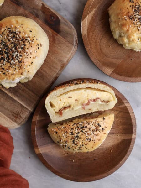 Breakfast pockets sitting on wood plates, with one cut open, showing the middle stuffed with eggs, bacon and cheese.