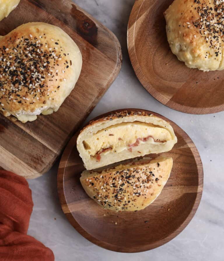 Breakfast pockets sitting on wood plates, with one cut open, showing the middle stuffed with eggs, bacon and cheese.