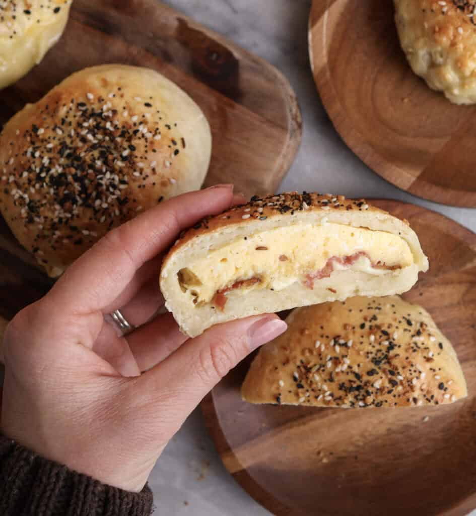 A hand holding a breakfast pocket cut in half, showing the fluffy scrambled eggs, bacon and eggs.