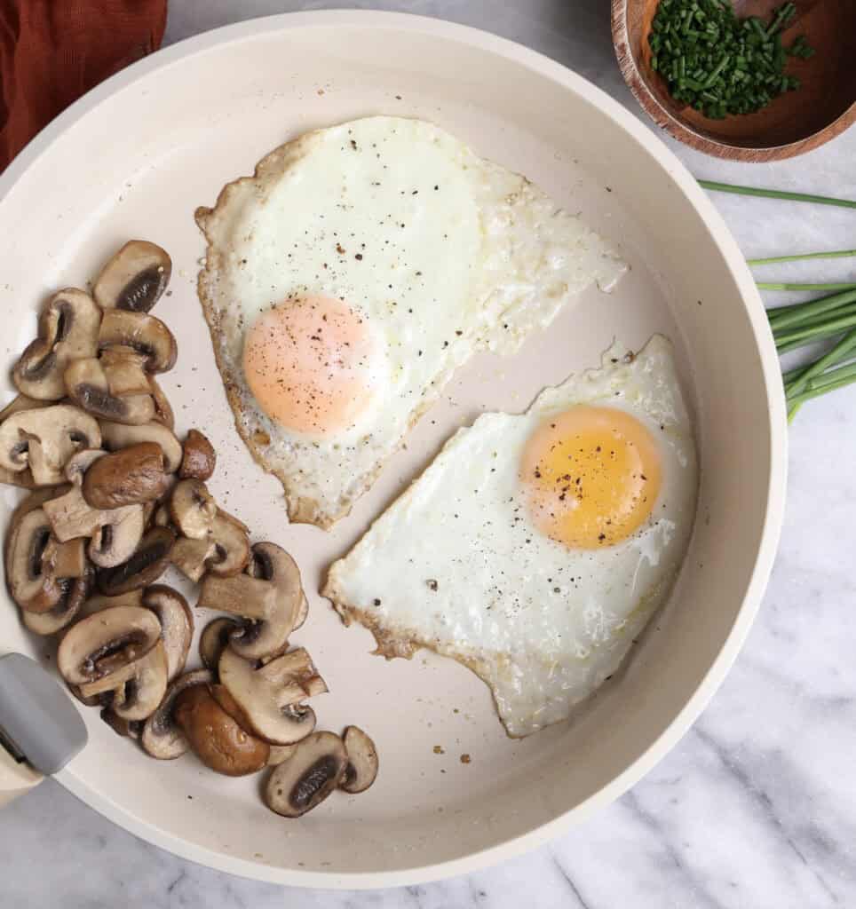 Fried eggs and sauteed mushrooms in a skillet.