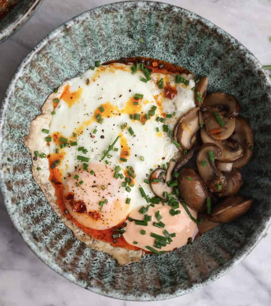 Savory oatmeal bowl loaded with fried egg, mushrooms and spicy sriracha mayo.